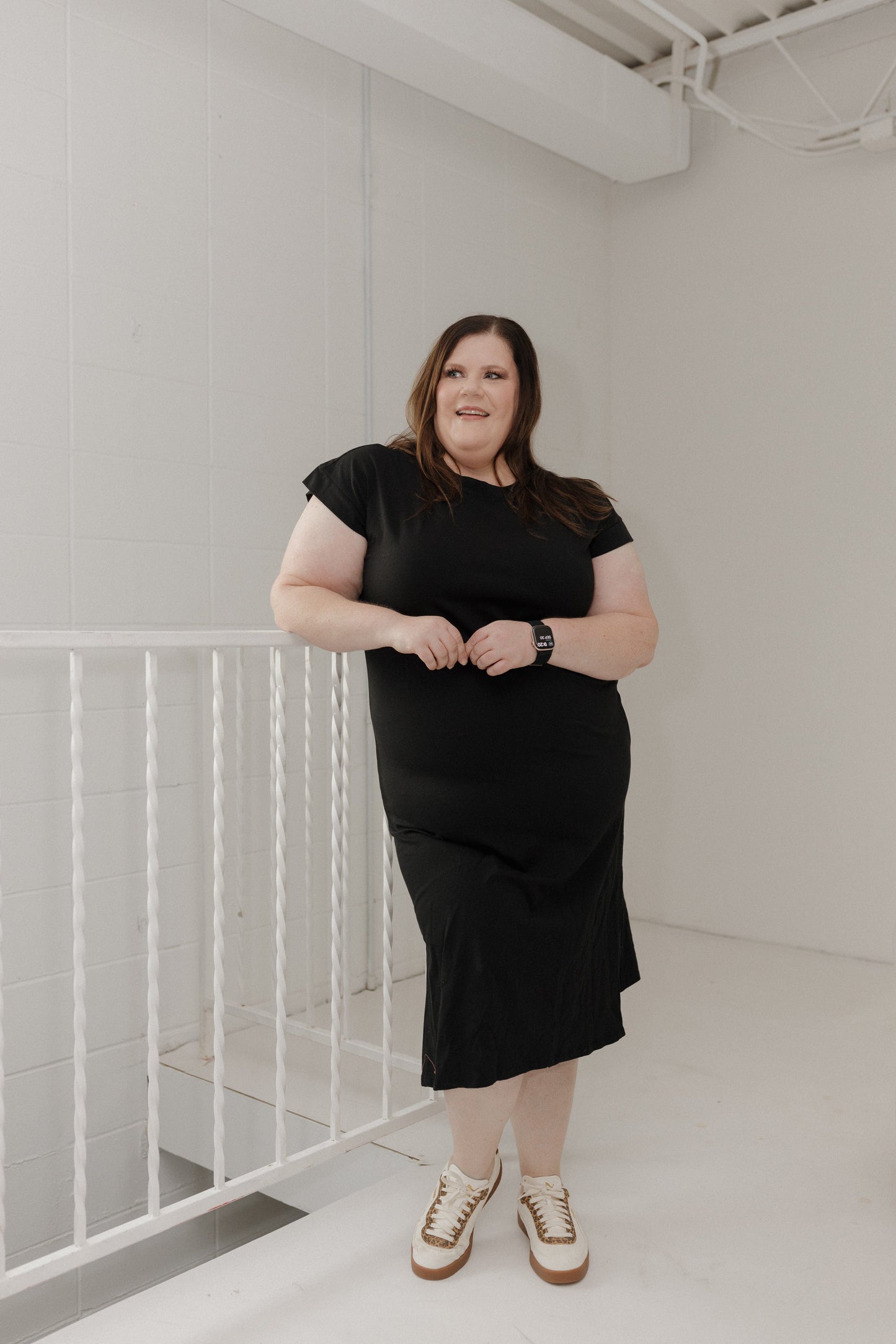 Person wearing a black dress standing in a minimalistic room with white walls and floor.