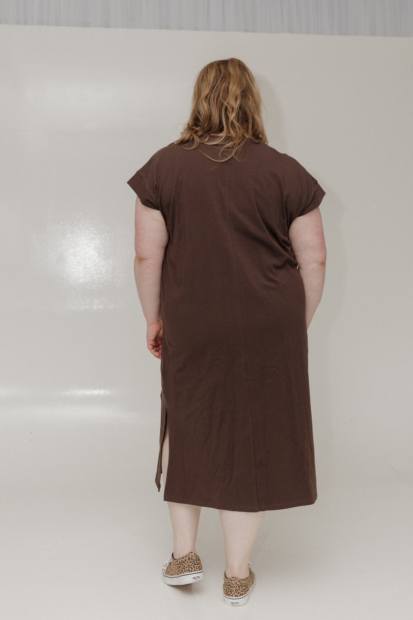 Person wearing a brown dress standing against a white wall