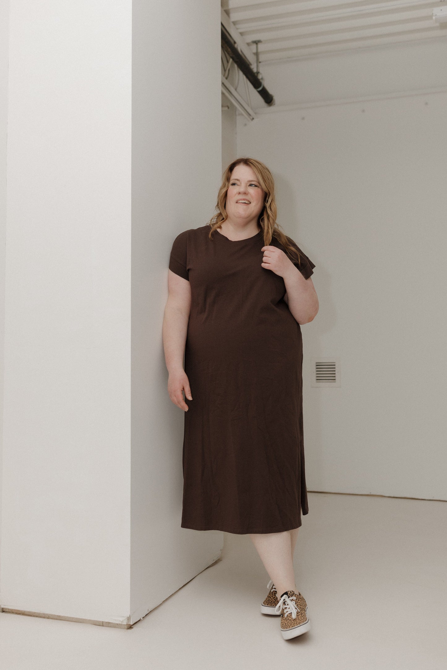 Woman wearing a brown dress standing against a white wall.