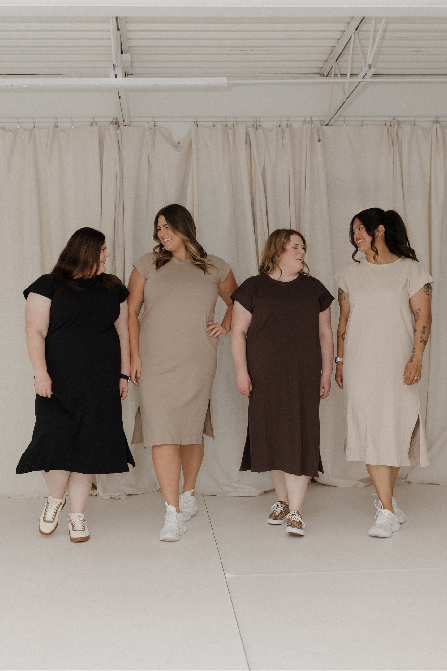 Four women wearing dresses standing in a line against a white curtain.