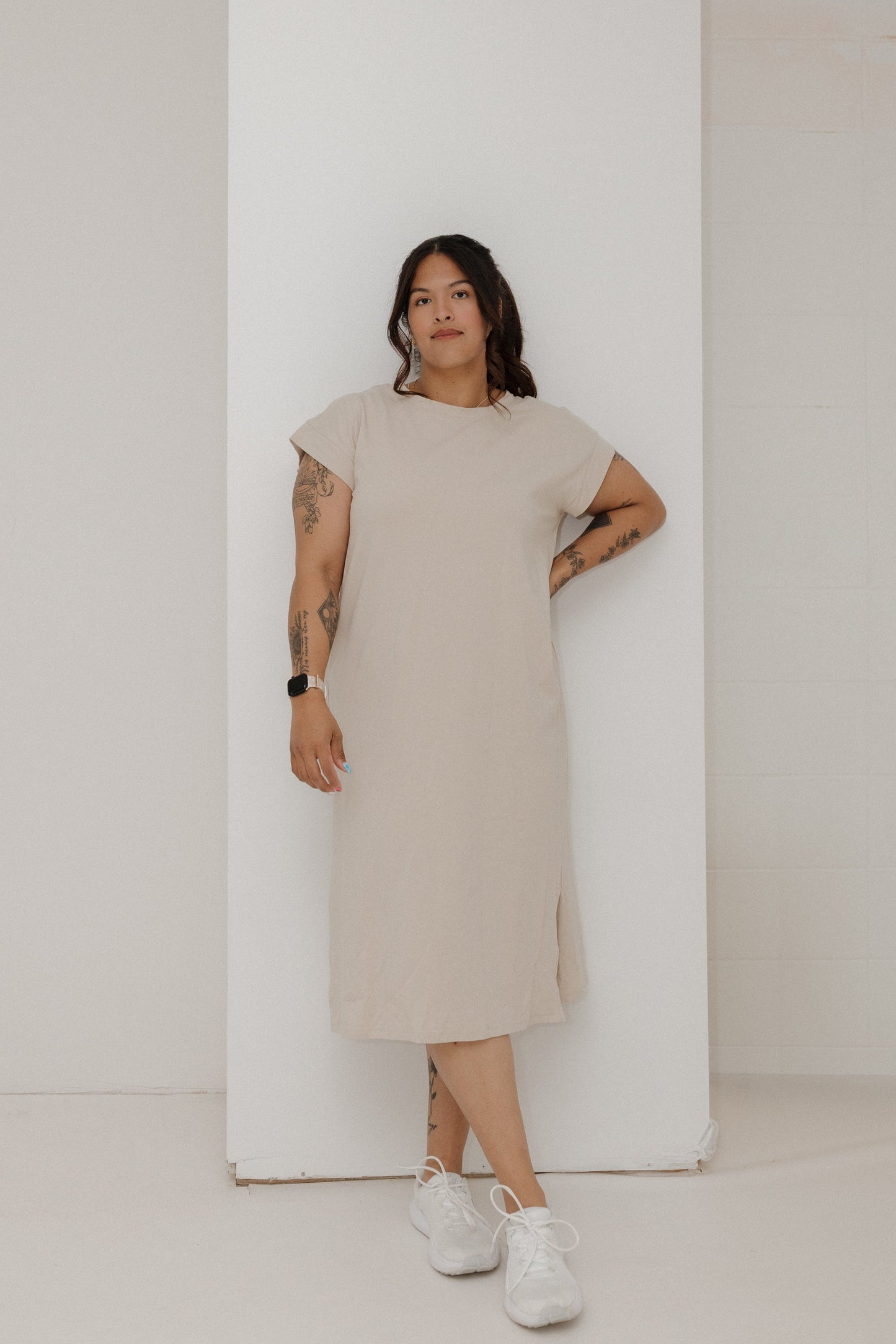 Woman wearing a beige dress standing against a white wall