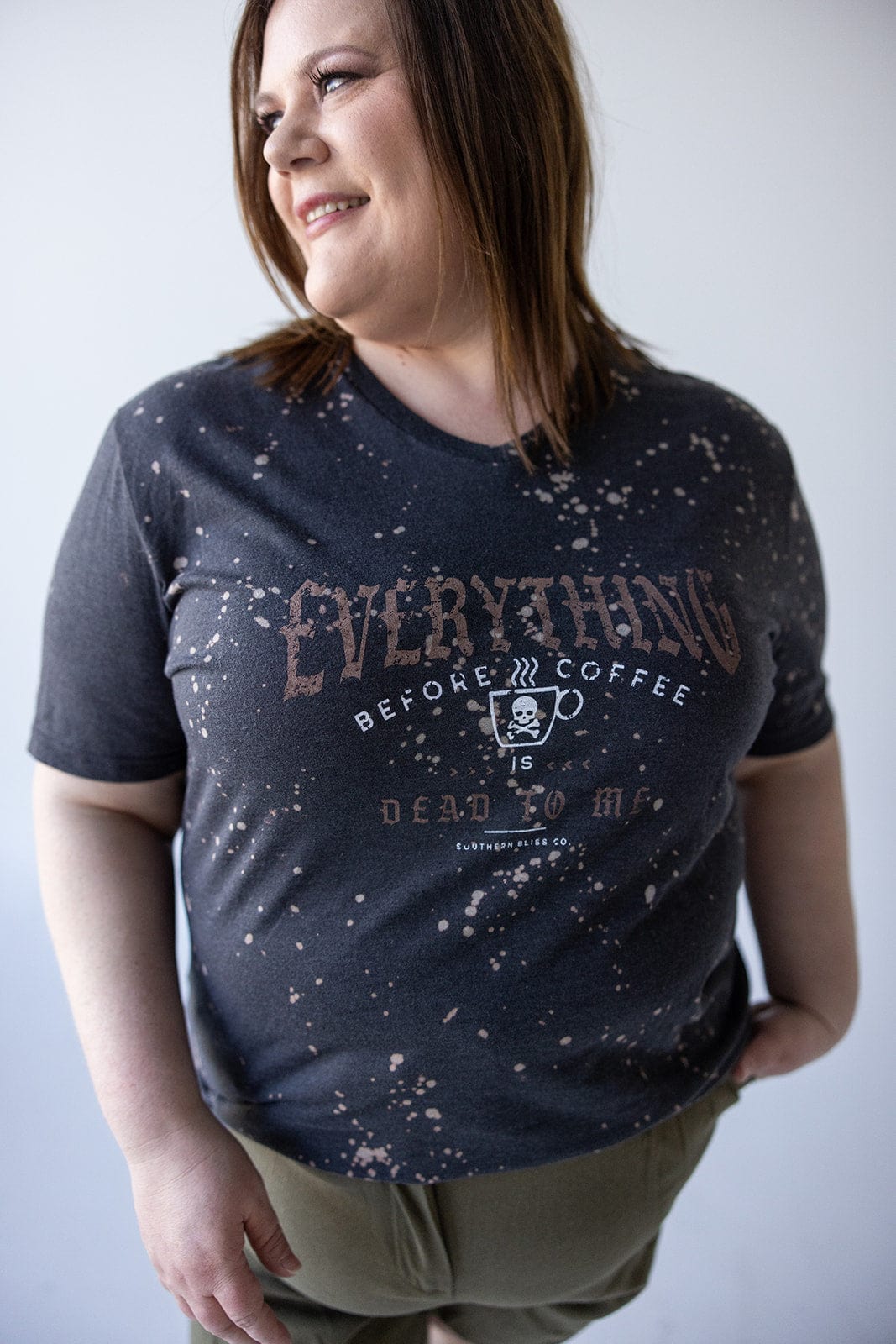 A person proudly wearing the Love Marlow "EVERYTHING BEFORE COFFEE IS DEAD TO ME" GRAPHIC TEE stands smiling with one hand on their hip.