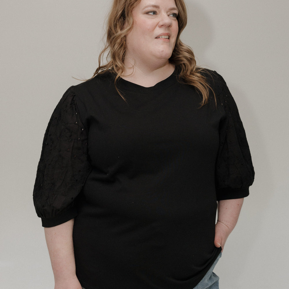 Person wearing a black top and light blue jeans against a plain background