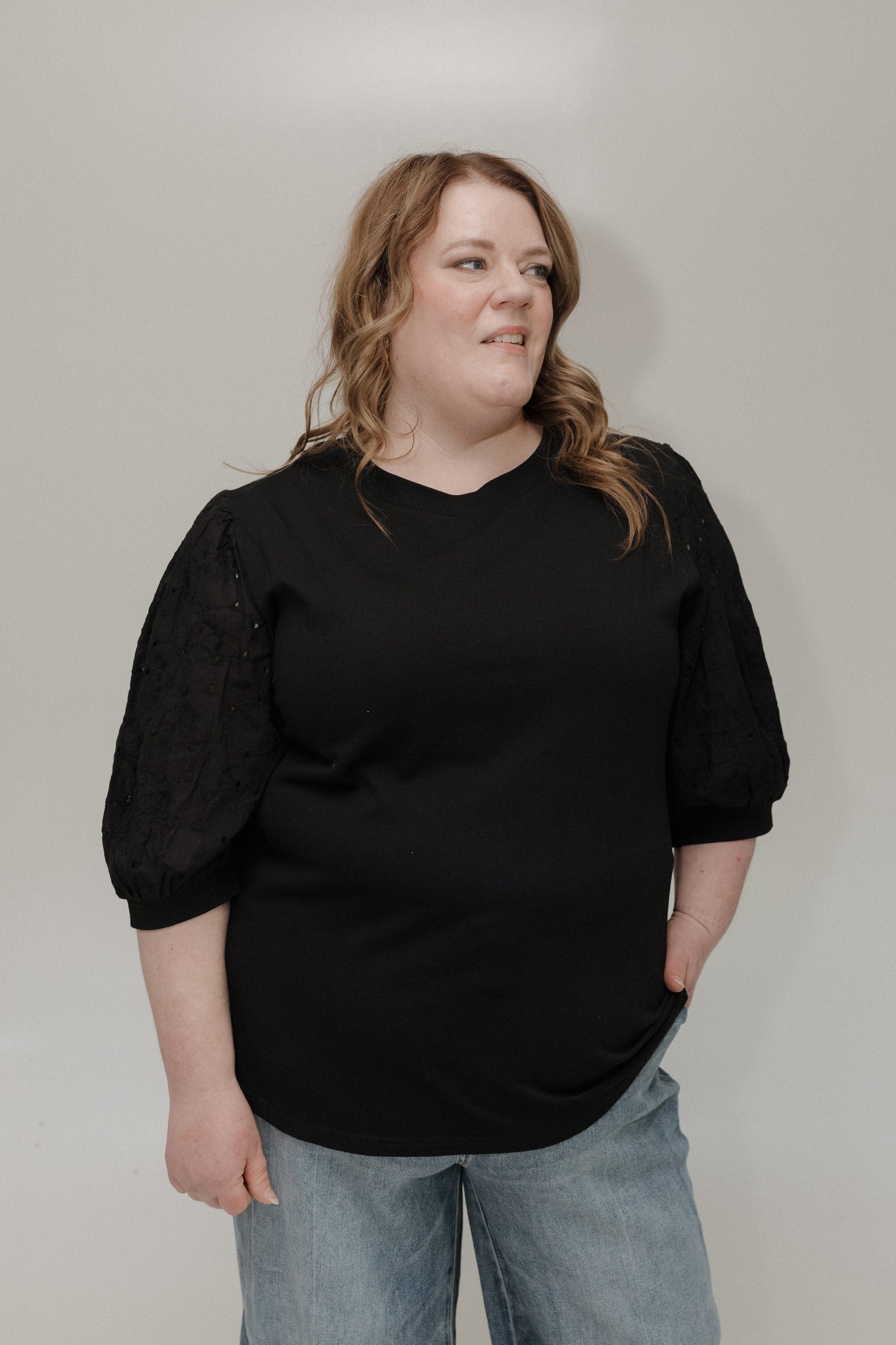 Person wearing a black top and light blue jeans against a plain background