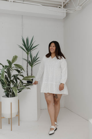 Woman in a white dress standing in a minimalistic room with plants.