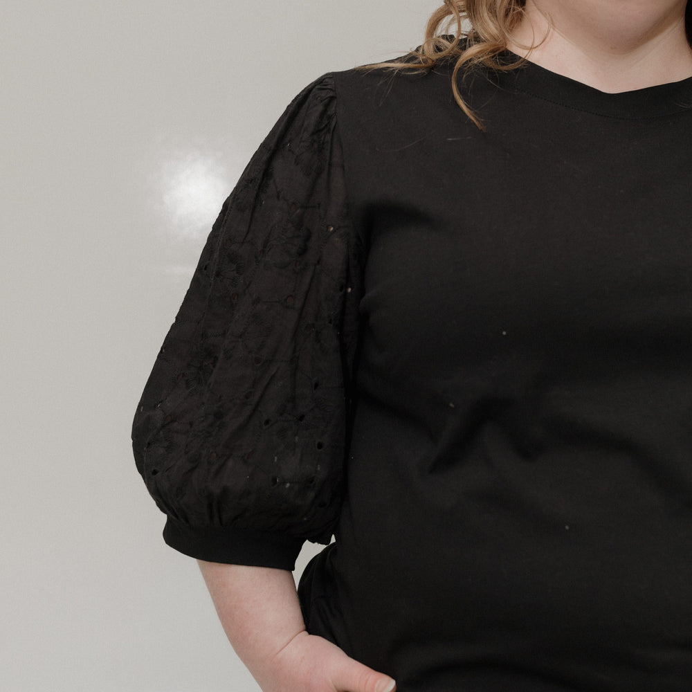 Person wearing a black blouse with puffed sleeves against a neutral background