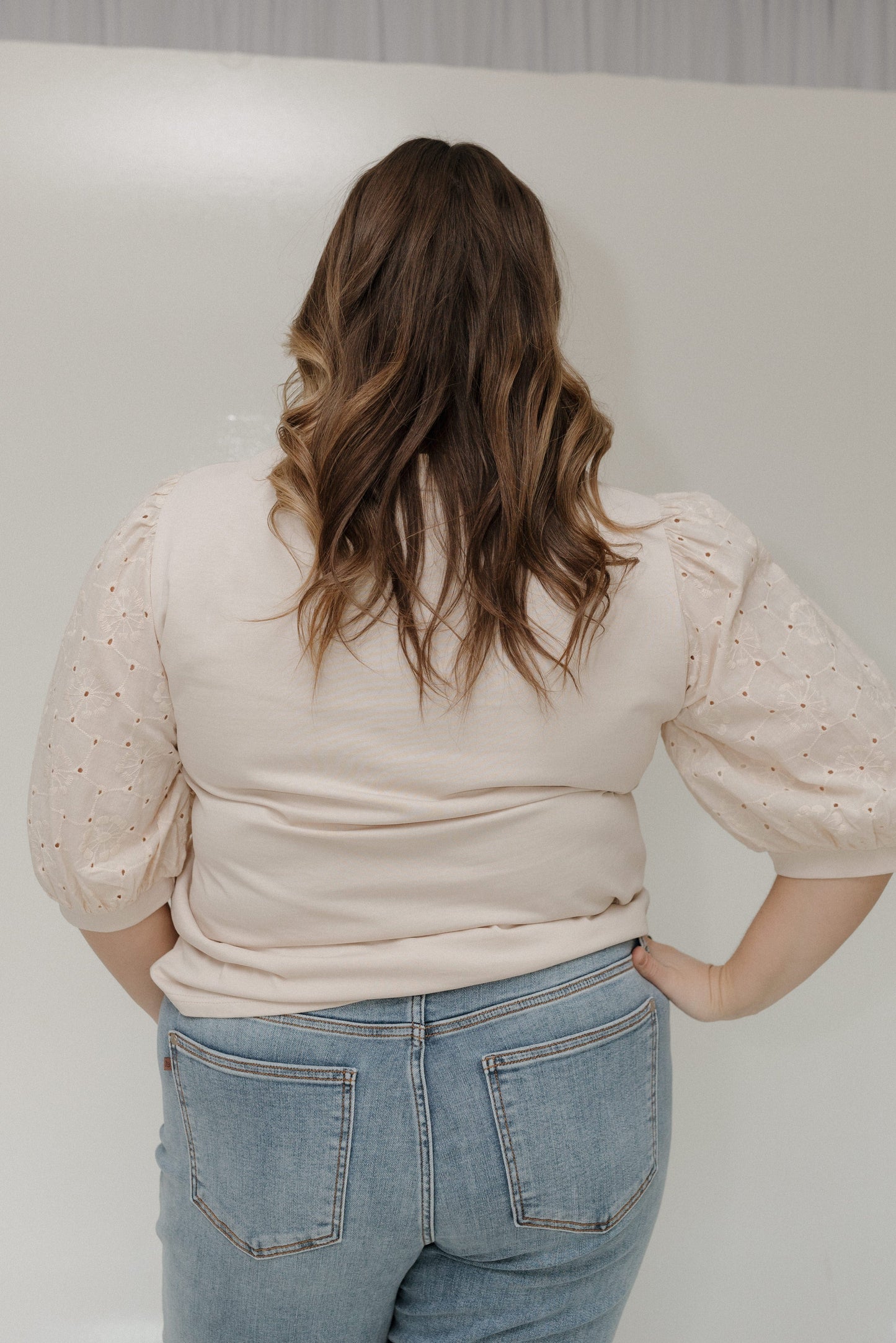 Person wearing a beige blouse and blue jeans against a plain background