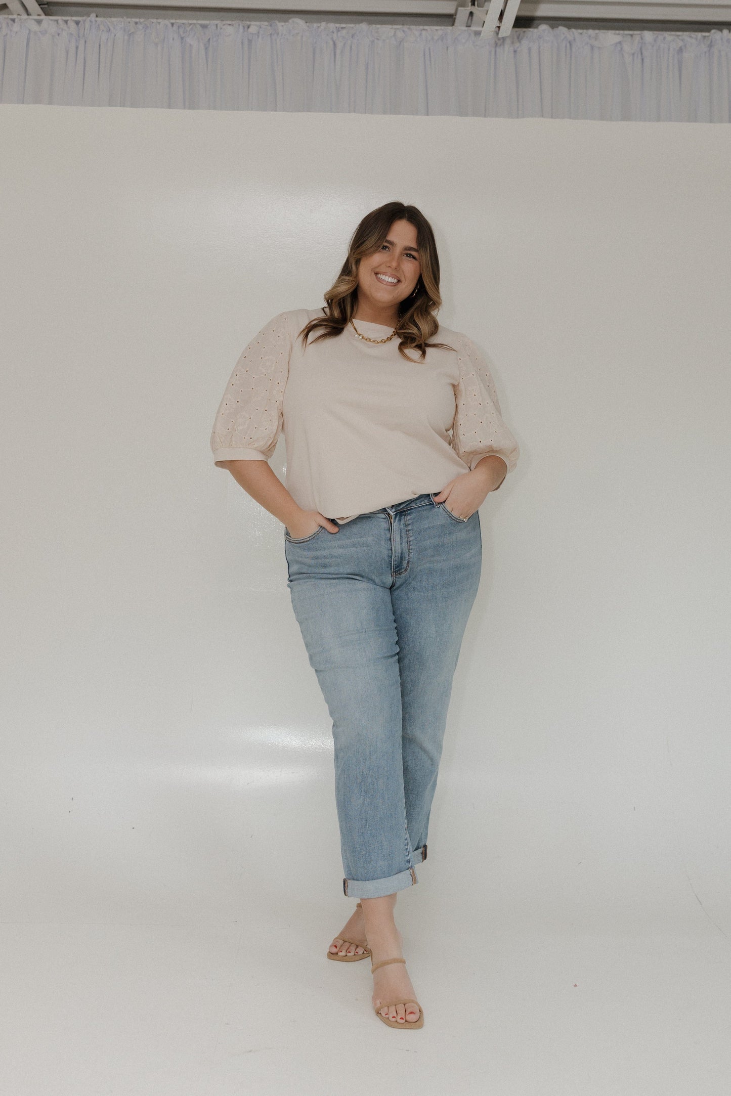 Woman wearing a beige blouse and light blue jeans standing against a white background