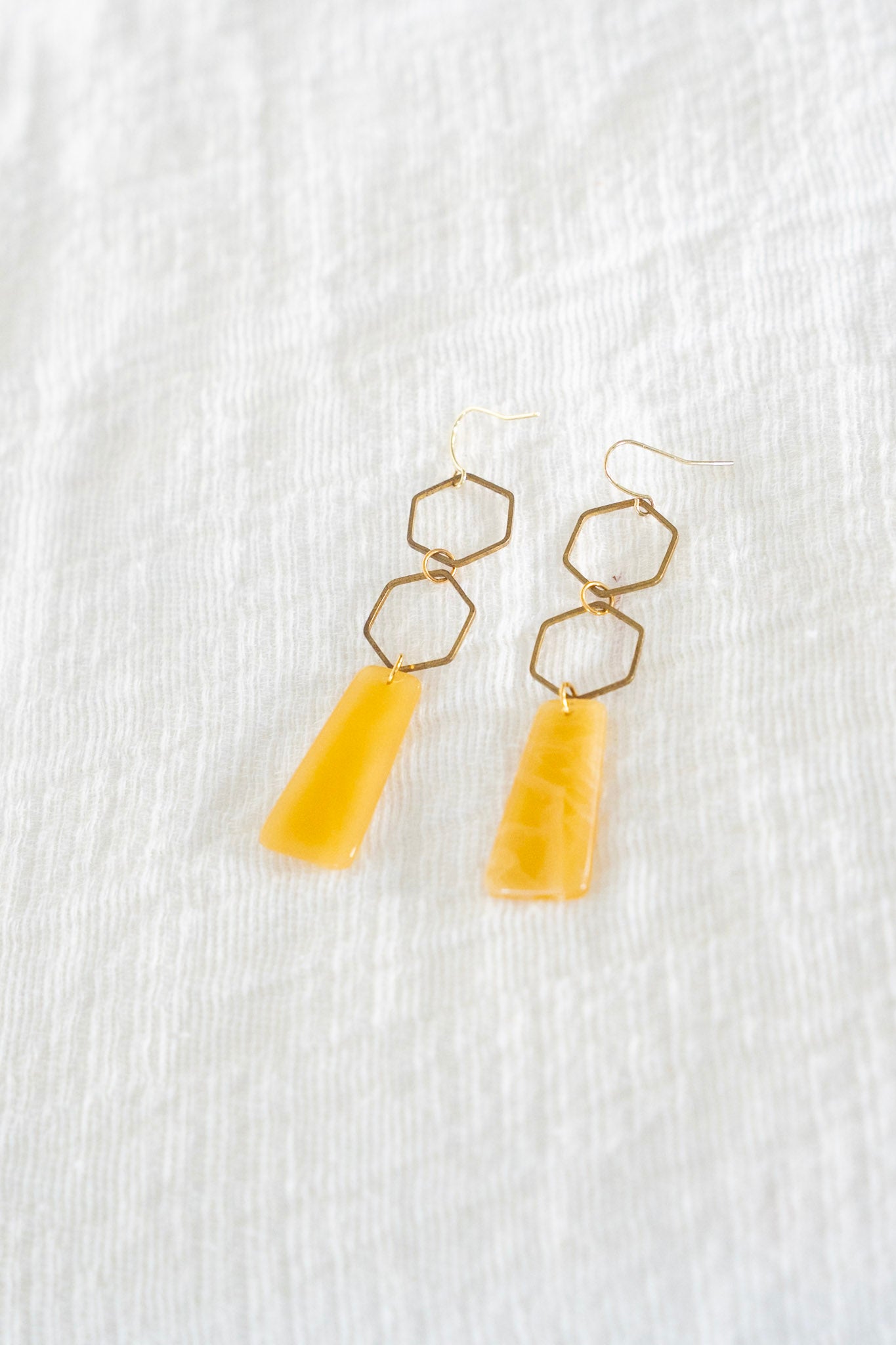 Yellow earrings with gold hexagonal tops on a white textured background
