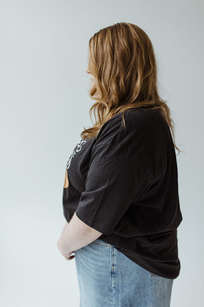 A person with long hair wearing Love Marlow's "Farm Fresh Pumpkins" graphic tee in black and a pair of jeans stands in profile against a plain background, ready for an autumn adventure.