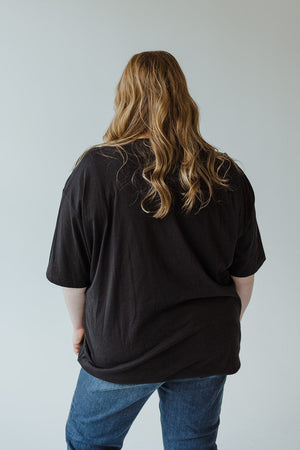 A person with long hair wearing the "Farm Fresh Pumpkins" with Truck Graphic Tee in Black by Love Marlow, featuring a super soft fabric, paired with jeans, facing away.