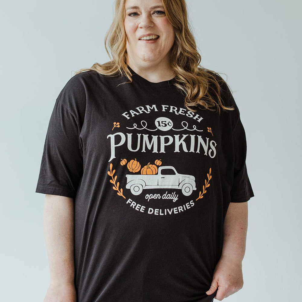 An individual wearing a Love Marlow Graphic Tee in super-soft fabric, showcasing pumpkins and a truck with the message "Farm Fresh Pumpkins, Open Daily, Free Deliveries.
