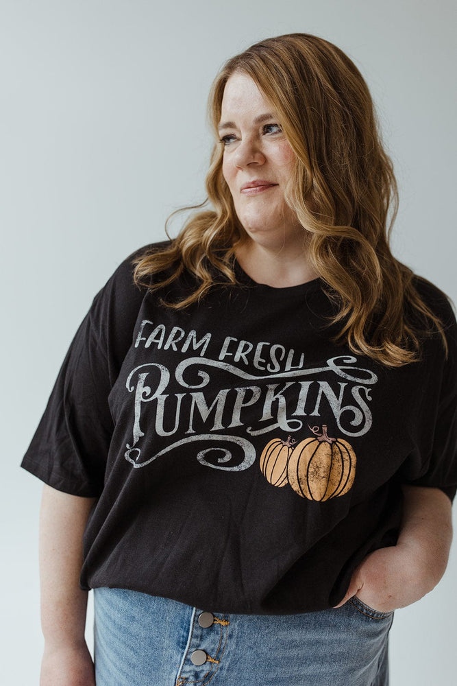 A person with long, wavy hair, wearing the "FARM FRESH PUMPKINS" graphic tee by Love Marlow in black and jeans crafted from super-soft fabric, is standing with their back to the camera, ready for an autumn adventure.