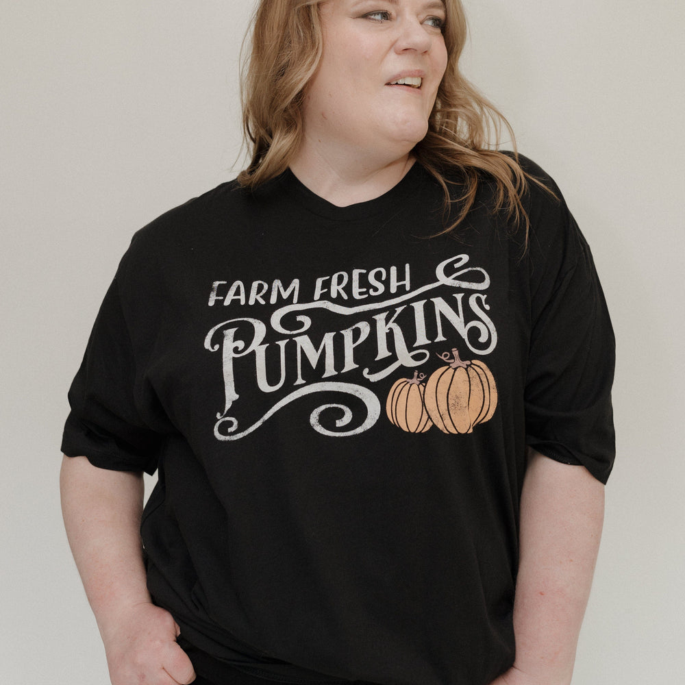 "FARM FRESH PUMPKINS" GRAPHIC TEE IN BLACK Woman wearing a black t-shirt with 'Farm Fresh Pumpkins' text and pumpkin graphic tee at Love Marlow