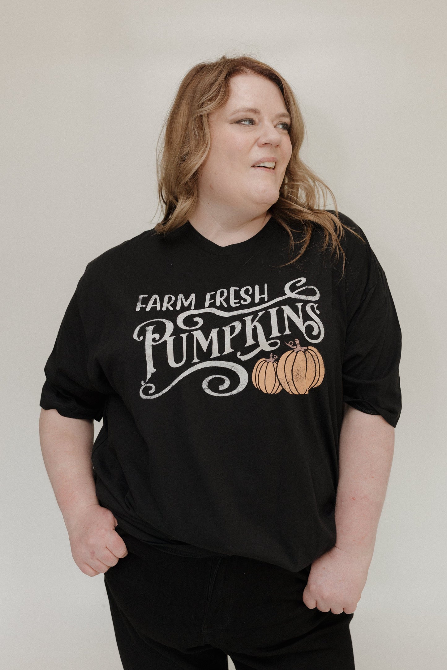 "FARM FRESH PUMPKINS" GRAPHIC TEE IN BLACK Woman wearing a black t-shirt with 'Farm Fresh Pumpkins' text and pumpkin graphic tee at Love Marlow
