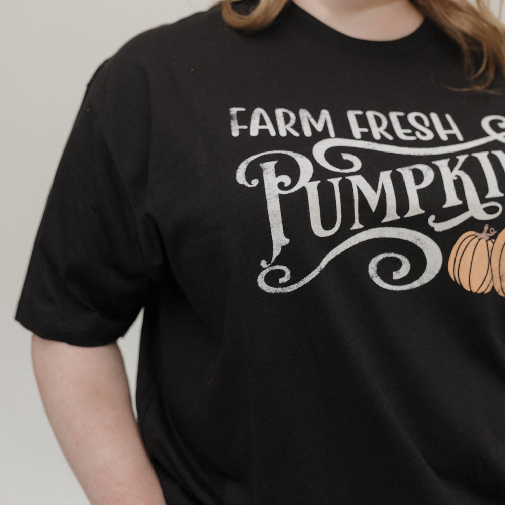 "FARM FRESH PUMPKINS" GRAPHIC TEE IN BLACK Woman wearing a black t-shirt with 'Farm Fresh Pumpkins' text and pumpkin graphic tee at Love Marlow
