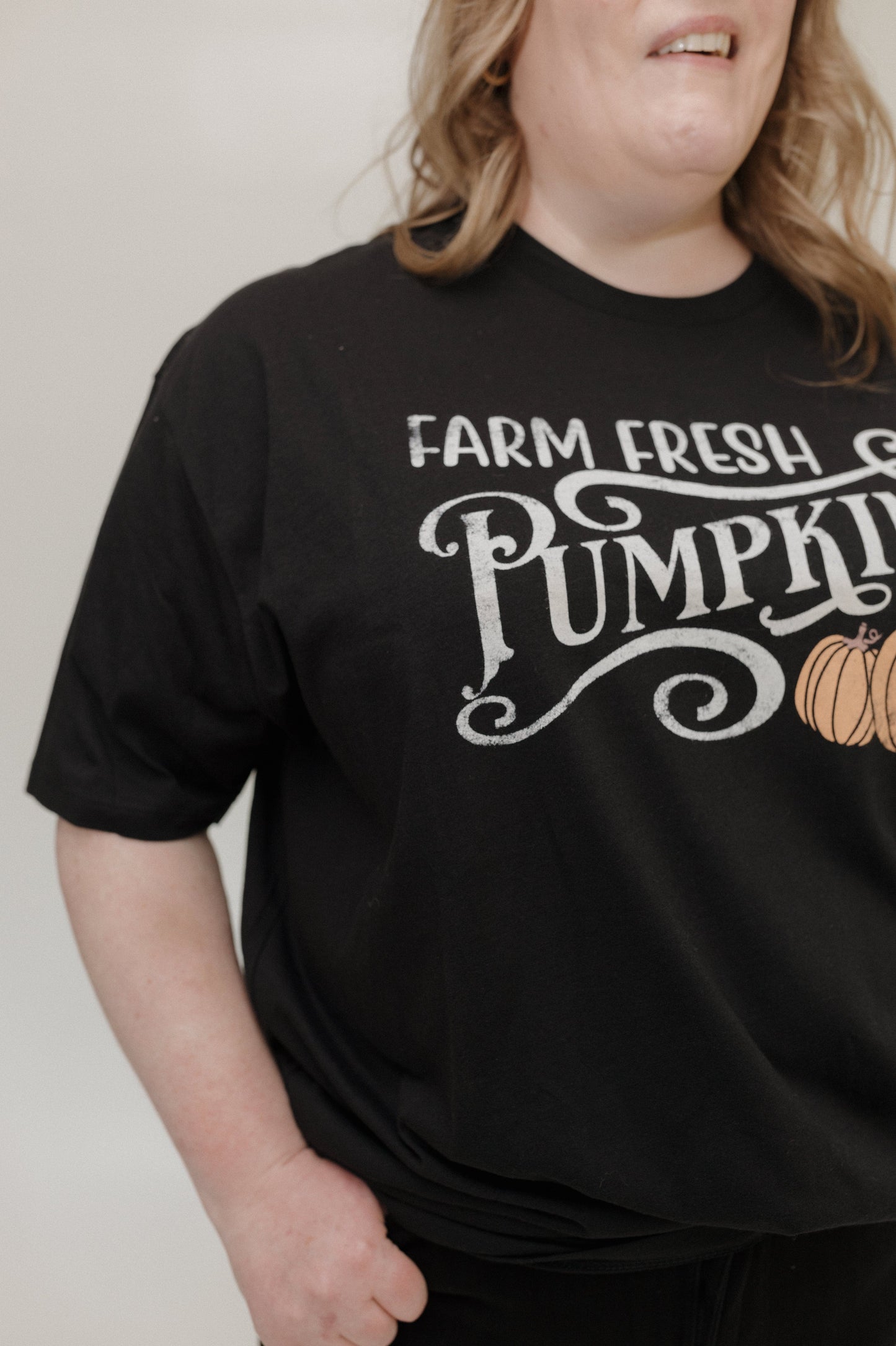 "FARM FRESH PUMPKINS" GRAPHIC TEE IN BLACK Woman wearing a black t-shirt with 'Farm Fresh Pumpkins' text and pumpkin graphic tee at Love Marlow