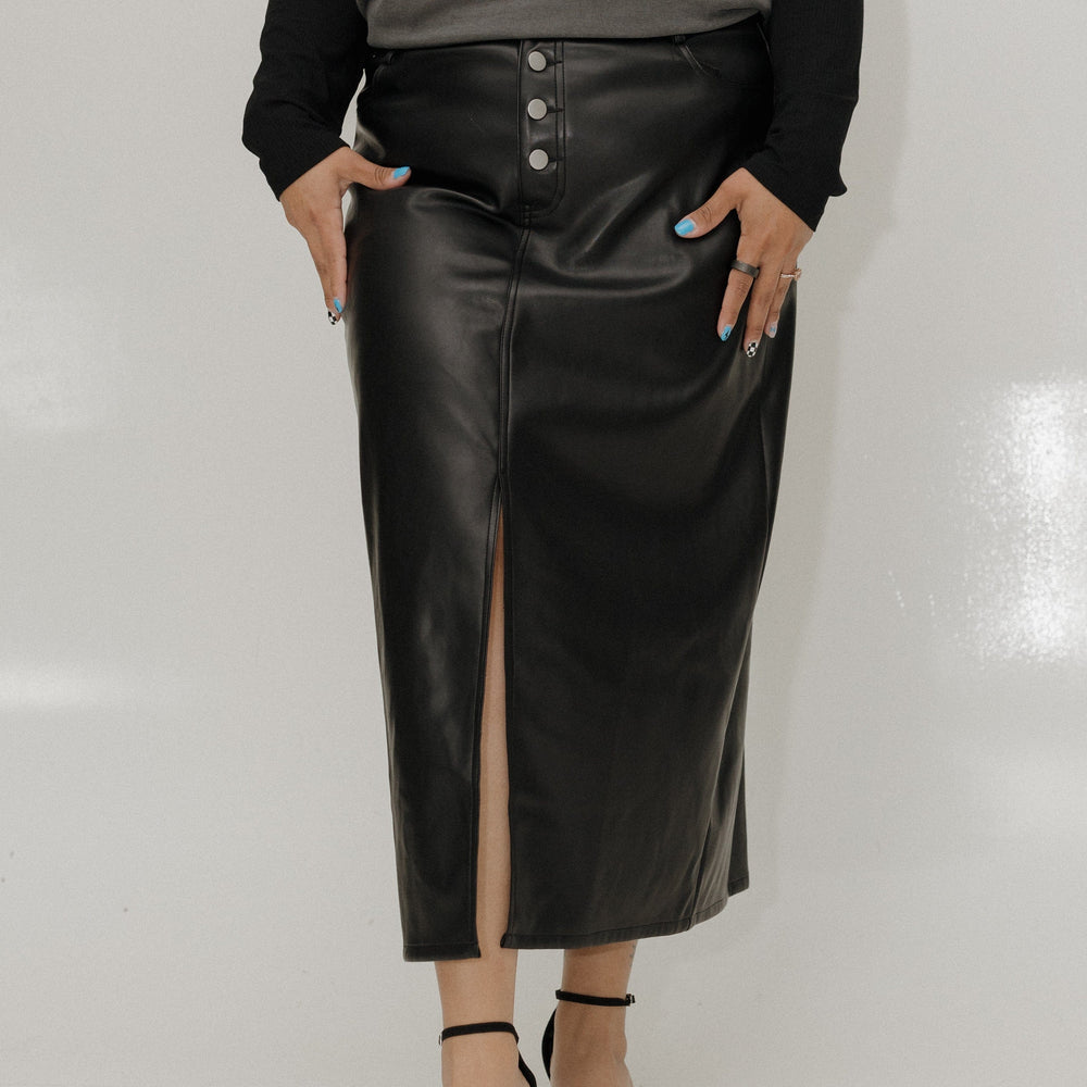 Person wearing a gray '90s hip hop' t-shirt, black leather skirt, and black sandals on a white background
