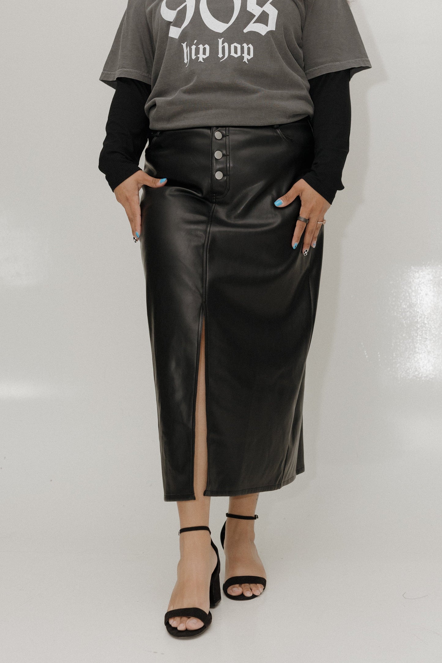 Person wearing a gray '90s hip hop' t-shirt, black leather skirt, and black sandals on a white background