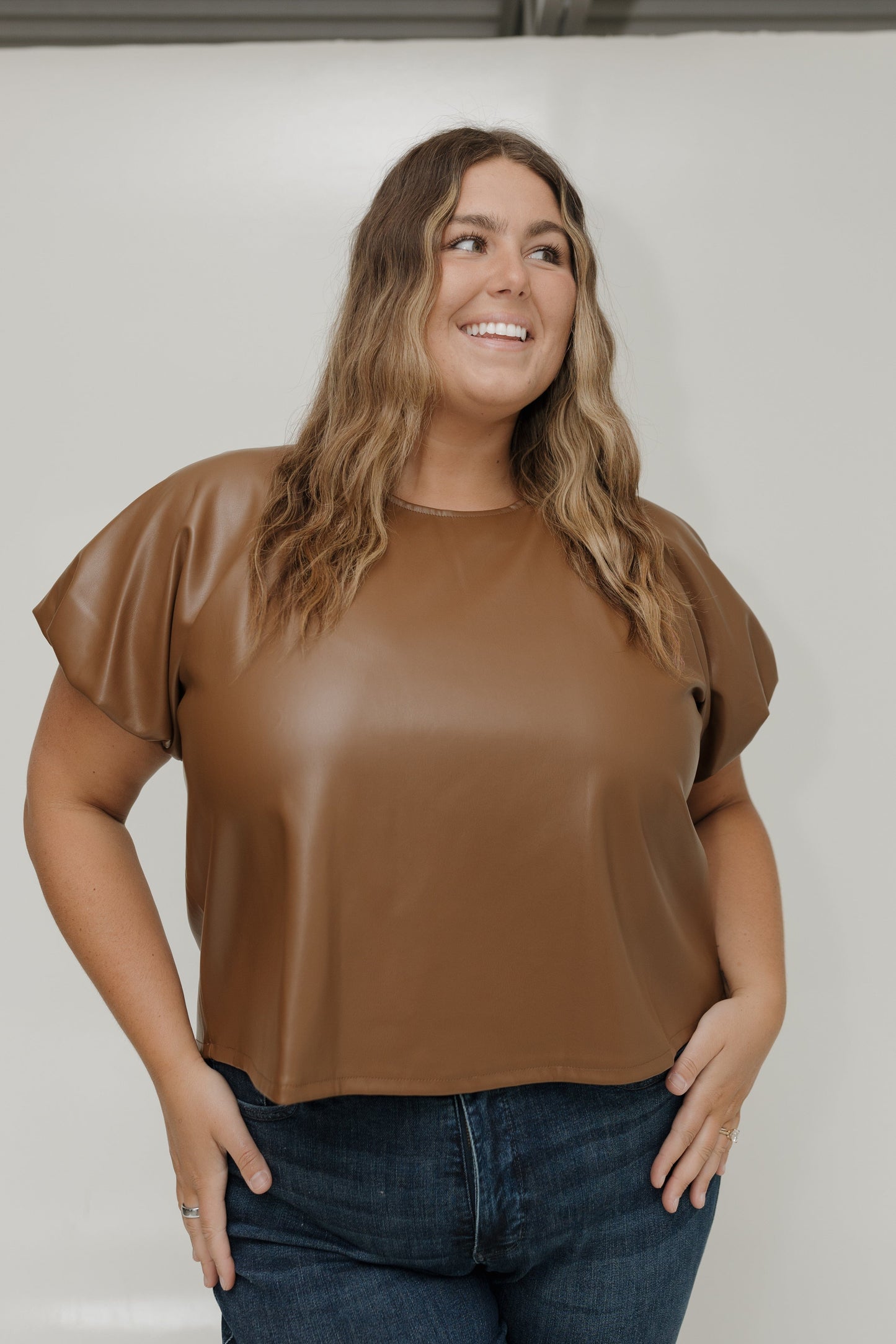Woman wearing a brown top and blue jeans against a white background