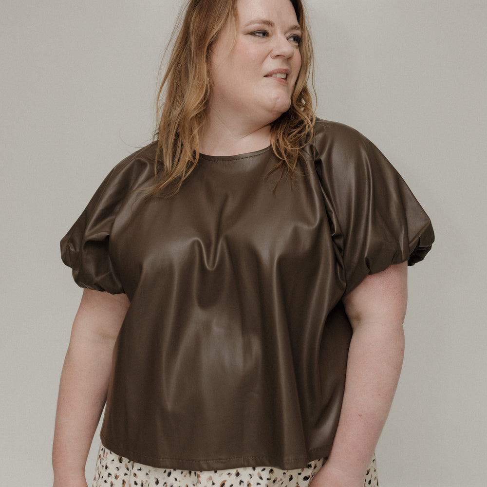 Woman wearing a brown satin top with puffed sleeves against a plain background