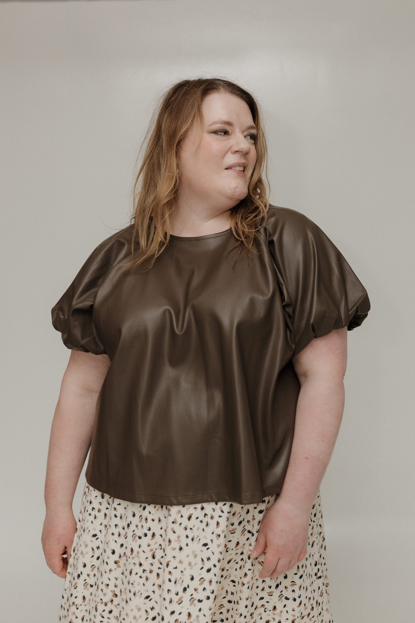 Woman wearing a brown satin top with puffed sleeves against a plain background