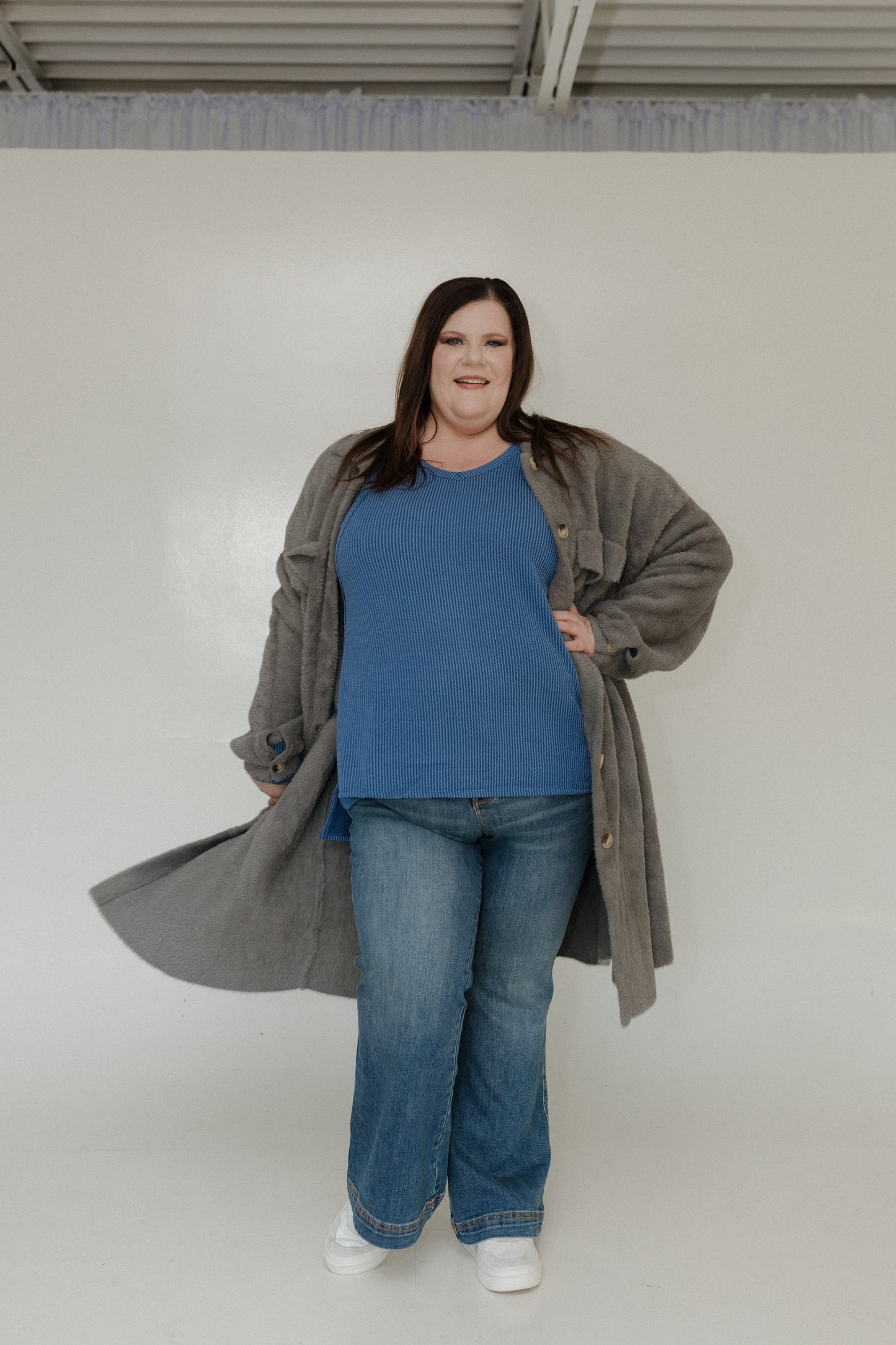 Person wearing a blue shirt, jeans, and a long gray coat against a white background