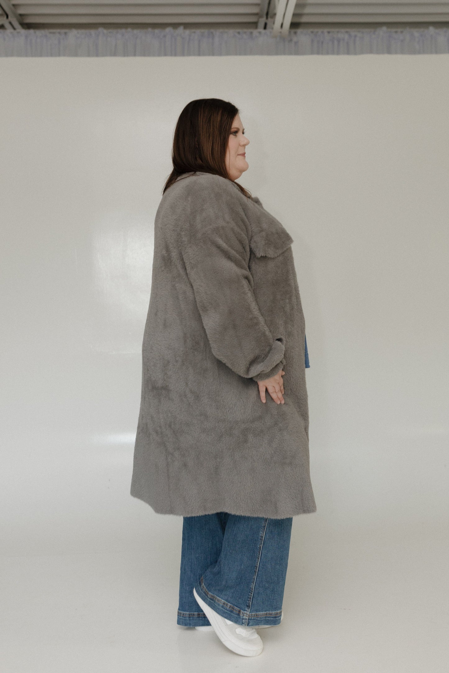 Person wearing a gray coat and blue jeans on a white background