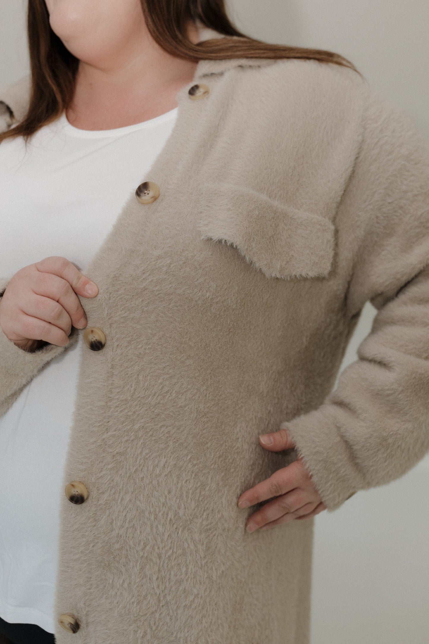 Person wearing a beige cardigan with buttons on a plain background