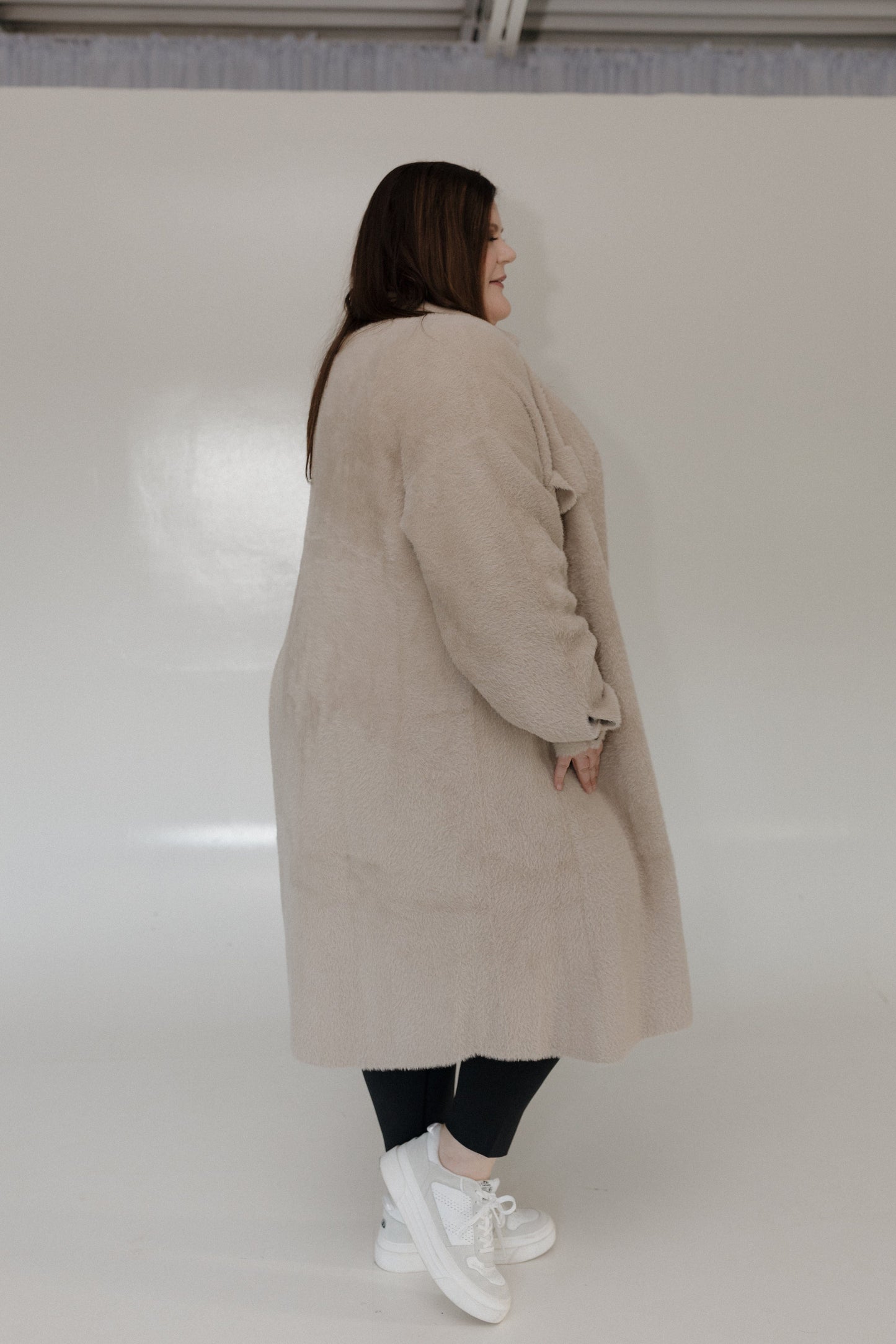 Person wearing a beige coat standing against a white background