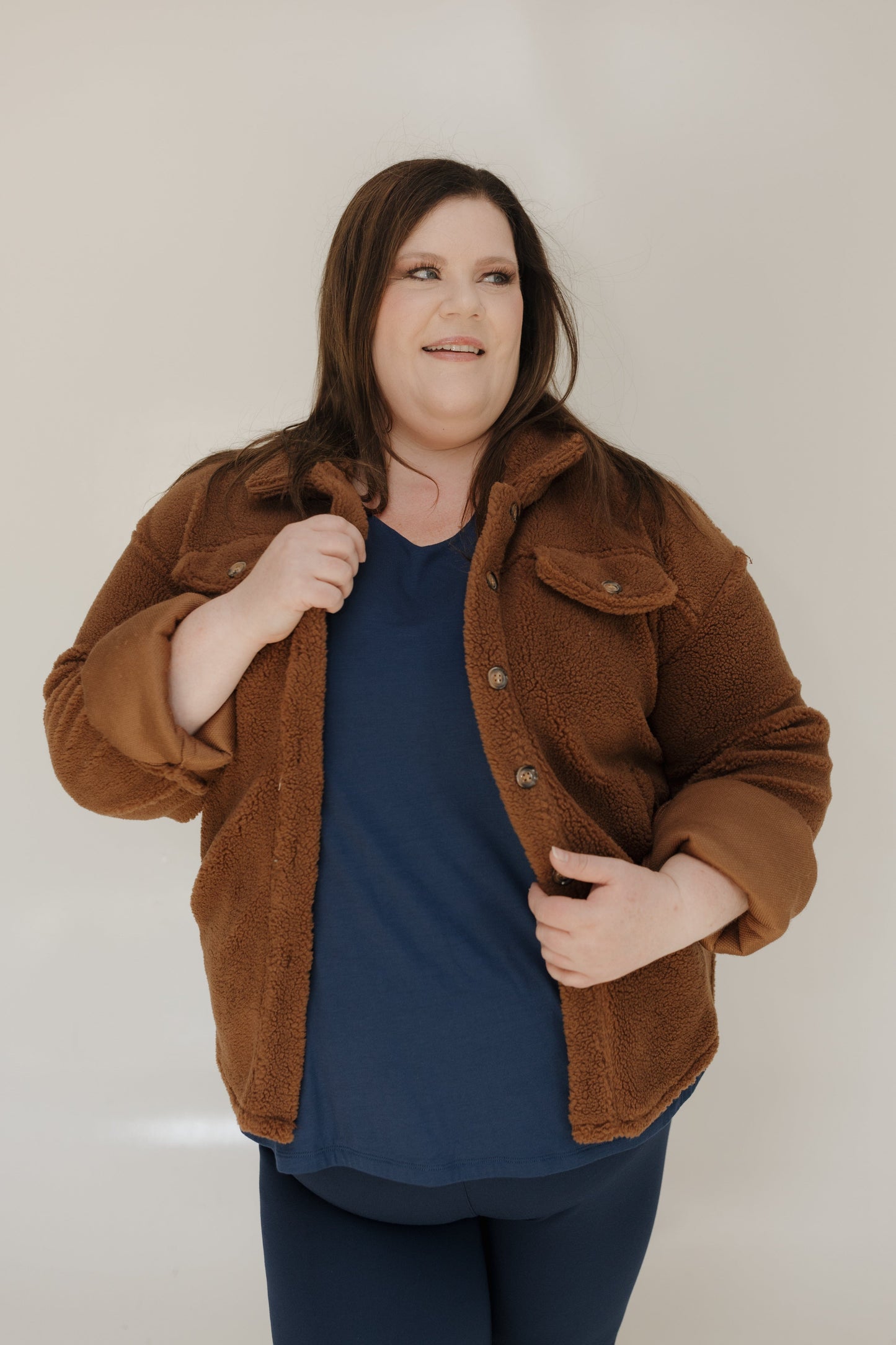 Woman wearing a brown jacket over a blue shirt against a plain background