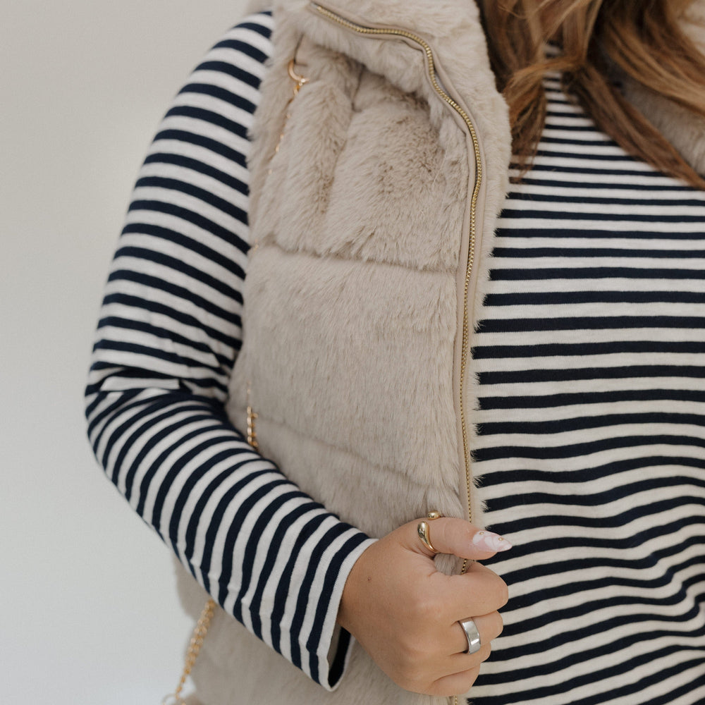Person wearing a striped shirt and beige vest against a neutral background