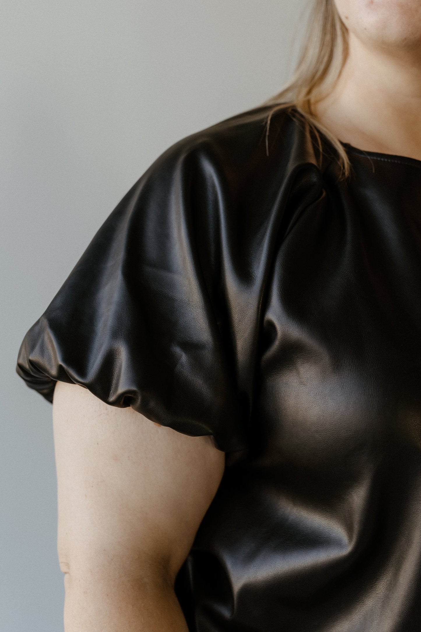 A person wearing a faux leather blouse with short, puffed sleeves stands against a plain background.