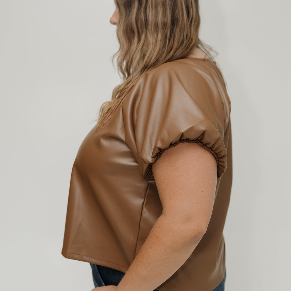 Woman wearing a brown leather-like top against a white background