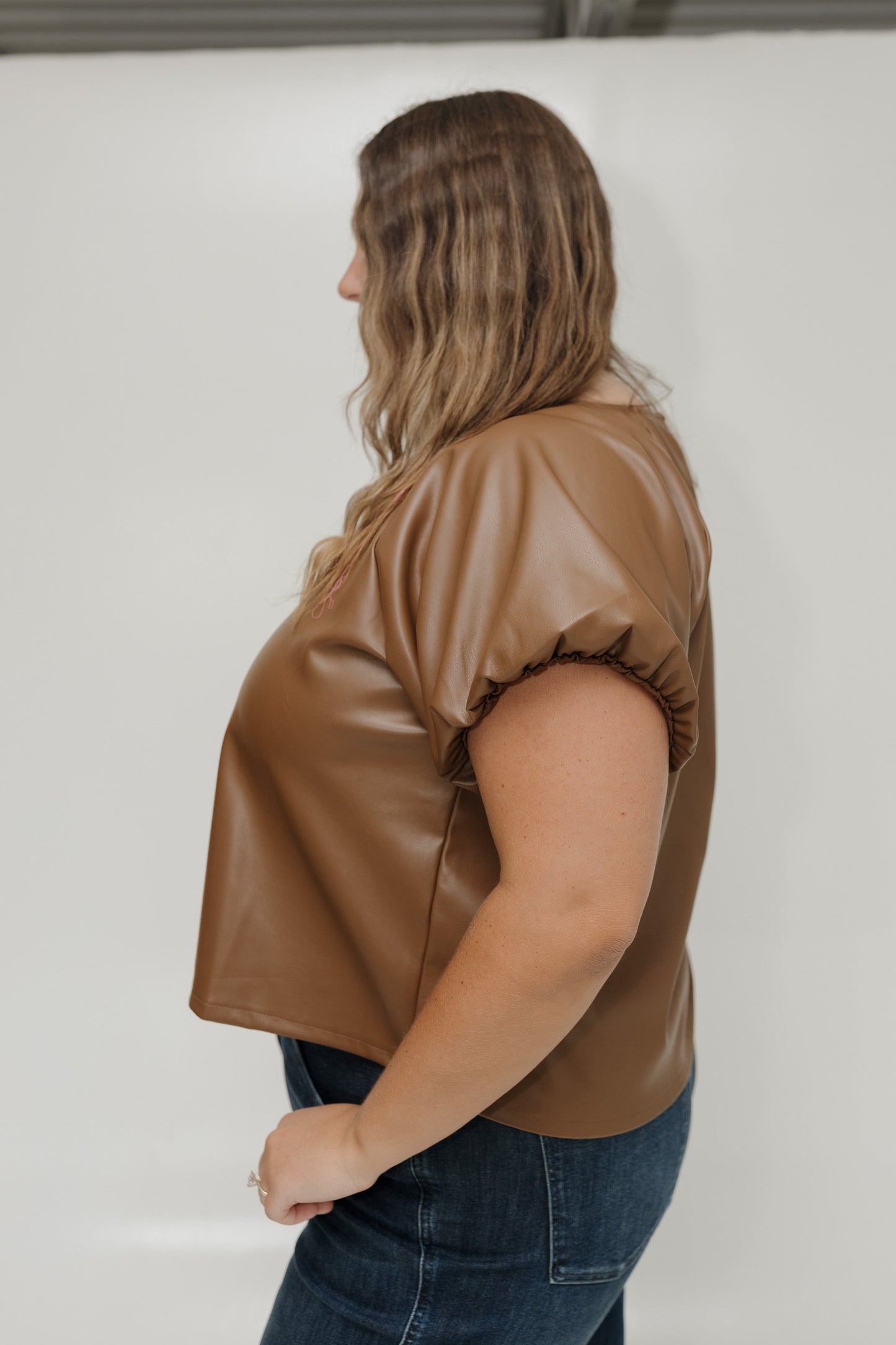 Woman wearing a brown leather-like top against a white background