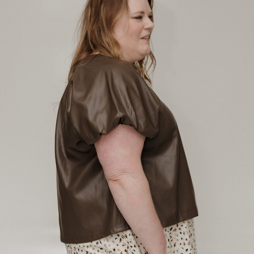 Woman wearing a brown satin top and patterned skirt against a plain background