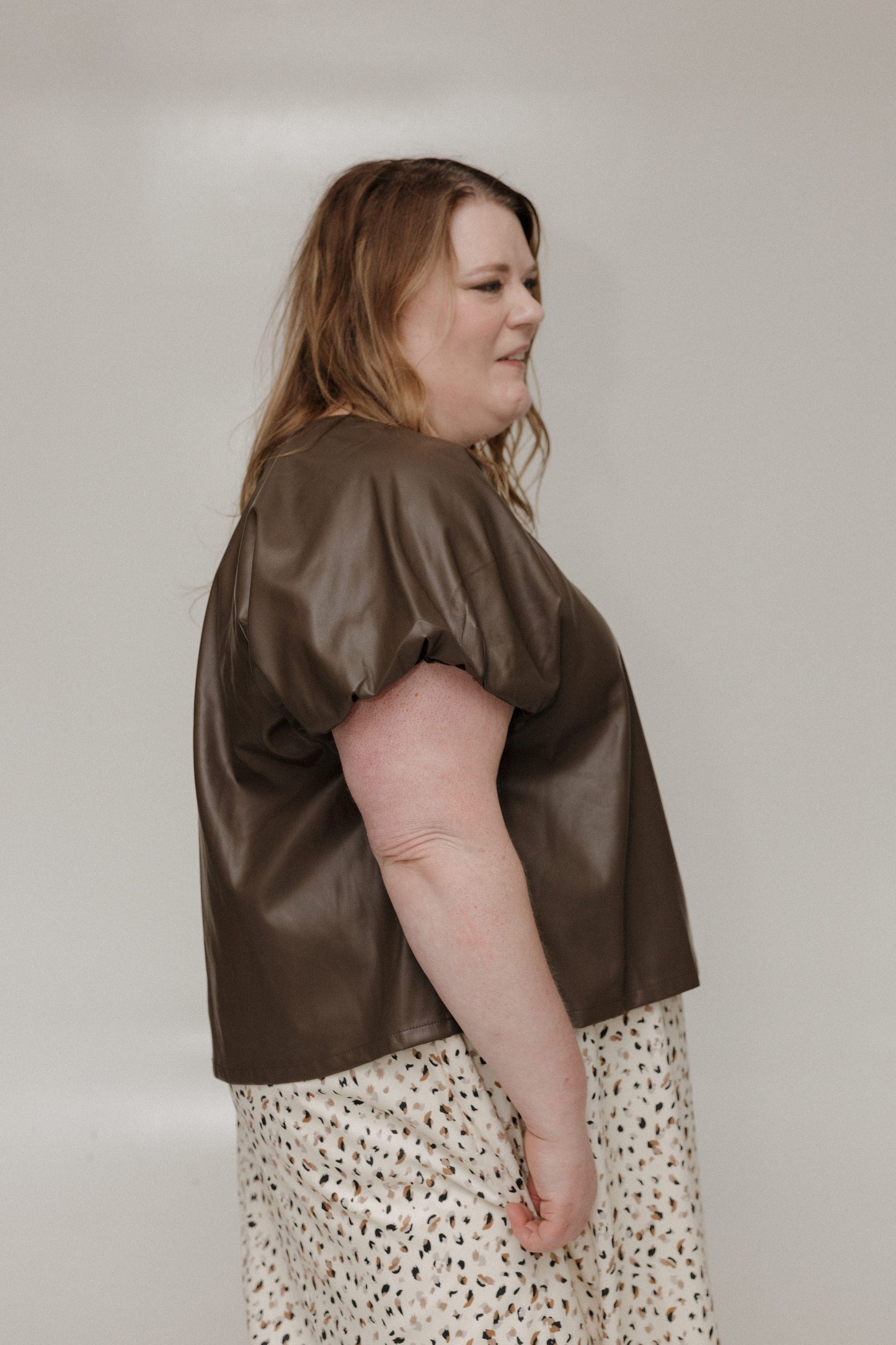 Woman wearing a brown satin top and patterned skirt against a plain background