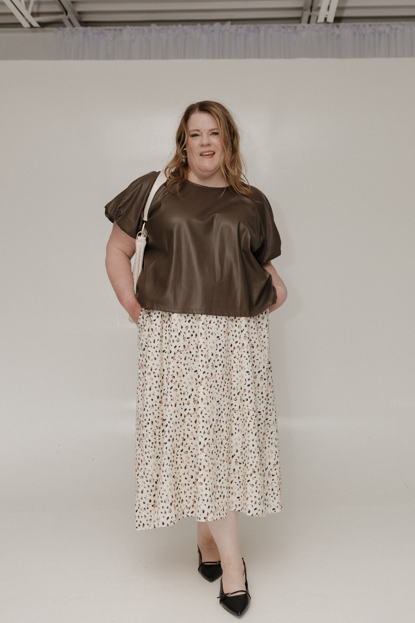 Woman wearing a brown top and floral skirt against a plain background