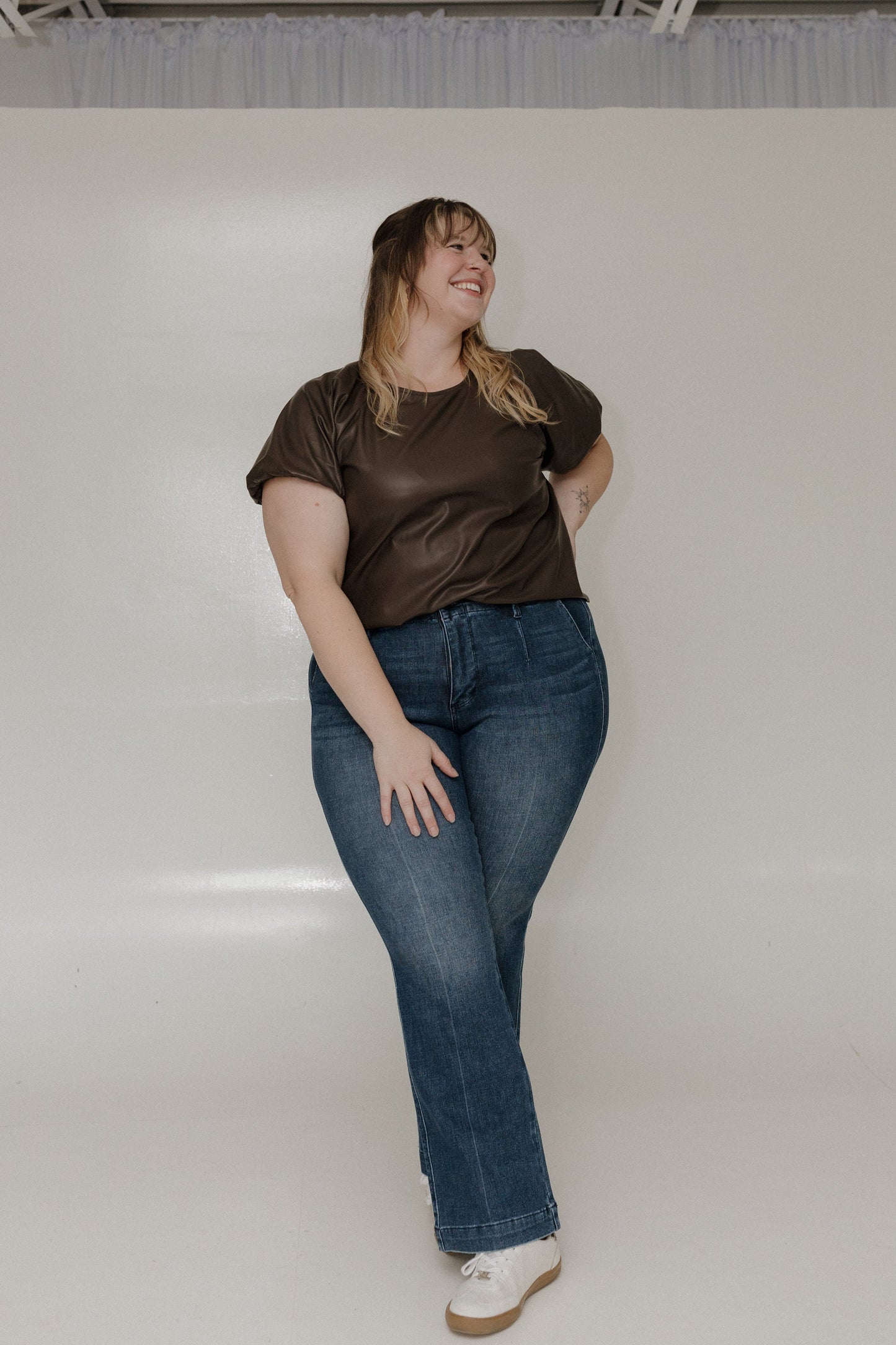 Woman wearing a brown shirt and blue jeans against a plain background