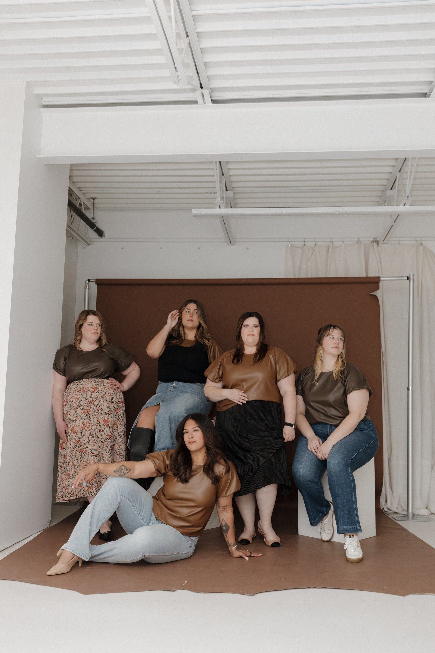 Five women posing together in a casual setting with a plain background