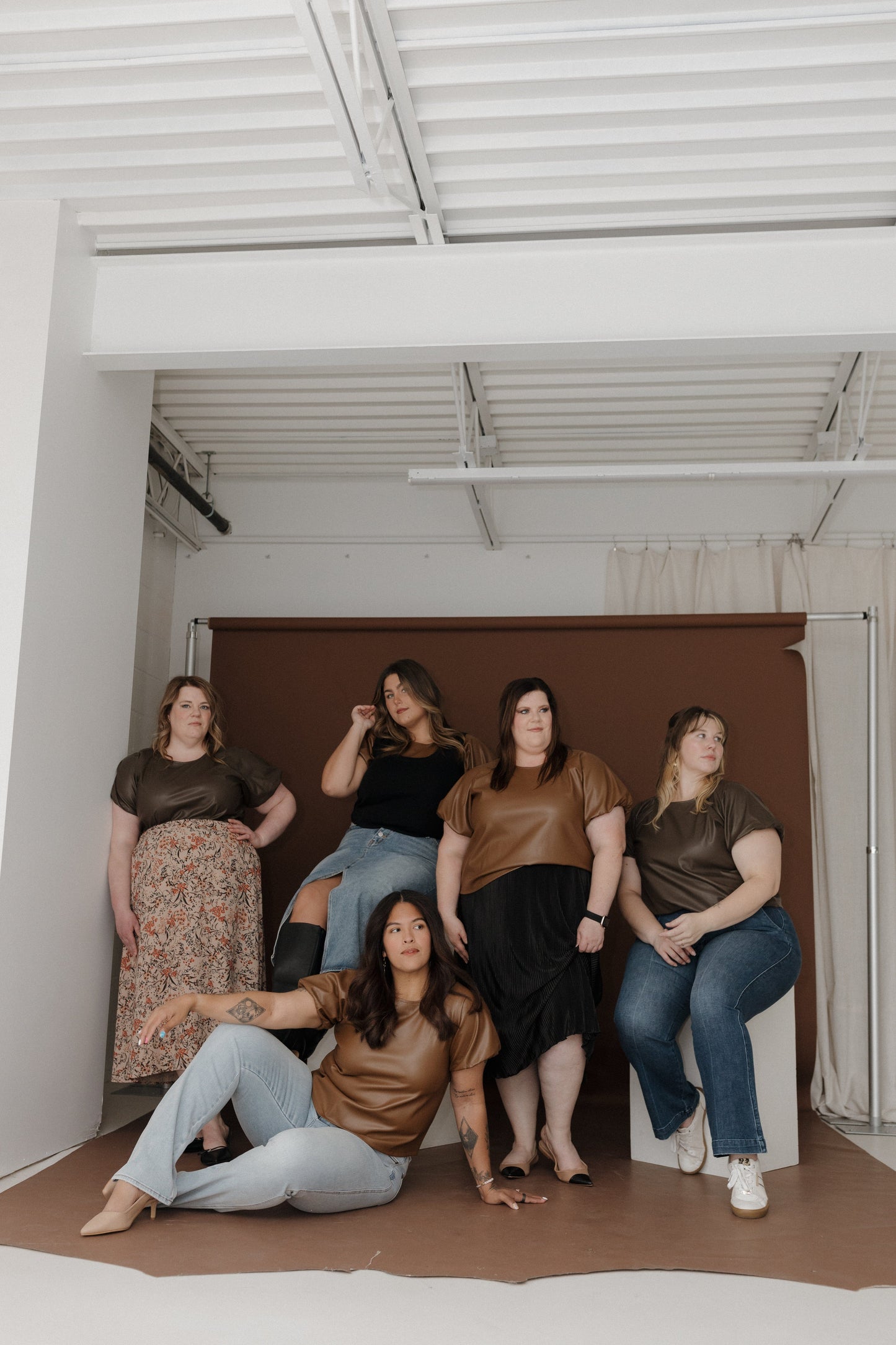 Five women posing together in a casual setting with a plain background