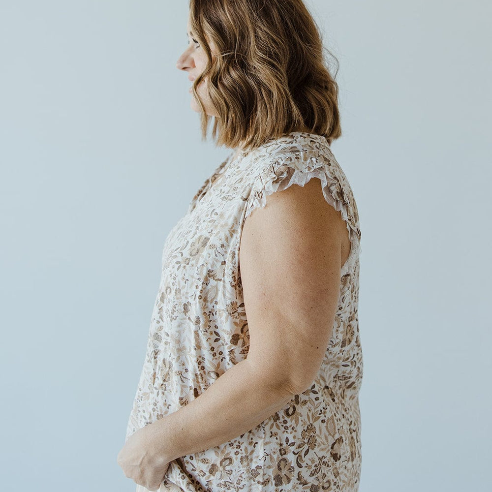 A woman with shoulder-length hair in a sophisticated, Love Marlow FEMININE CAP SLEEVE BLOUSE IN SAND and pleated skirt stands in profile against a plain background.