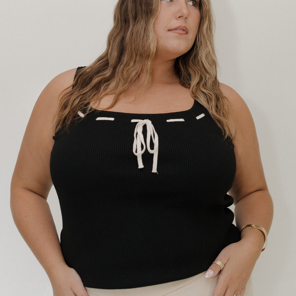 Woman wearing a black tank top with white accents against a plain background