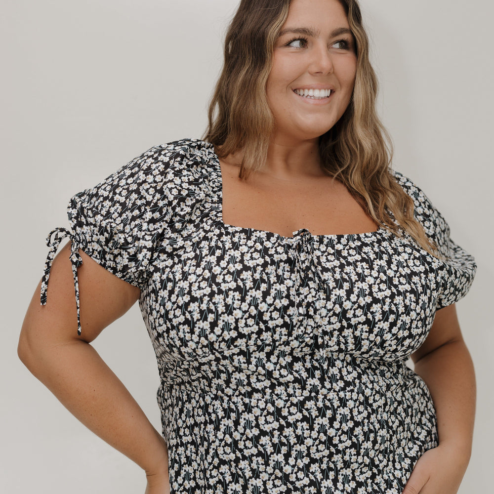 Woman wearing a black and white floral dress against a plain background