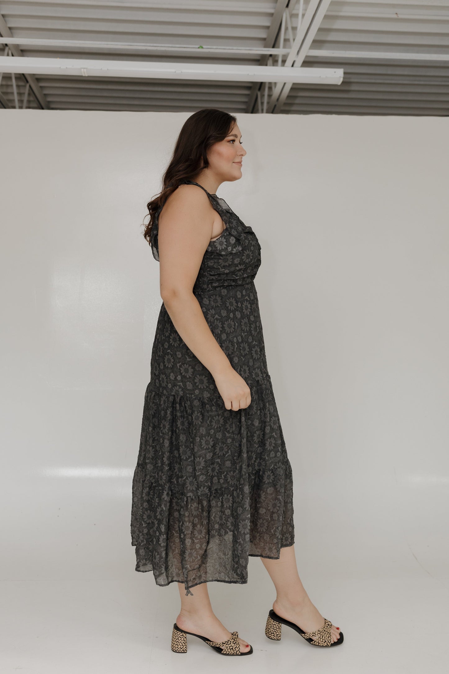 Woman wearing a dark floral dress standing against a white wall.