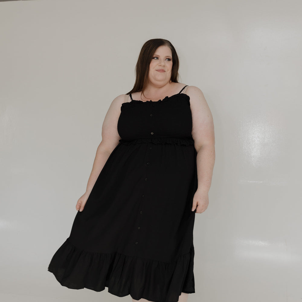 Woman wearing a black dress standing against a white wall.