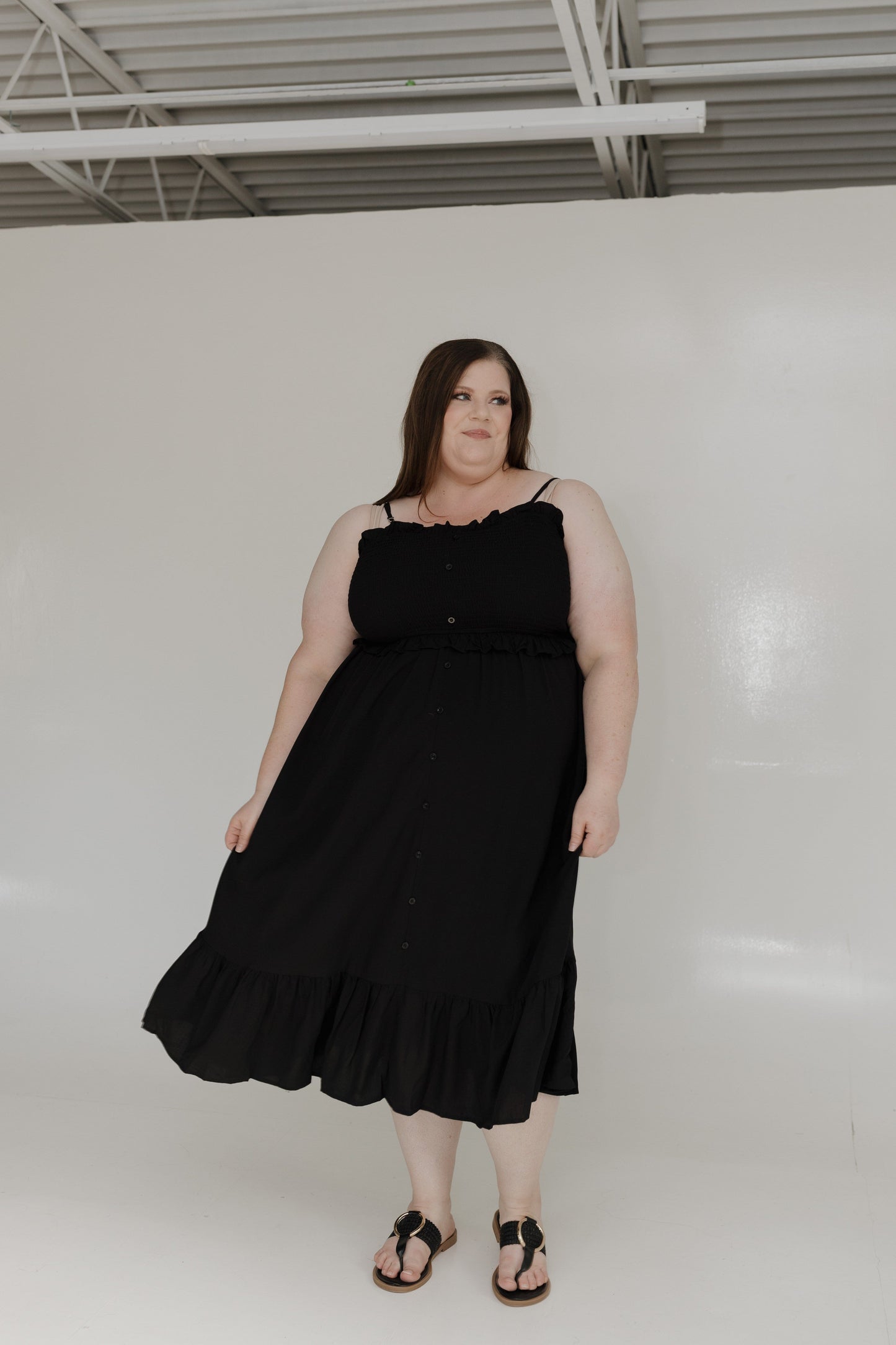 Woman wearing a black dress standing against a white wall.