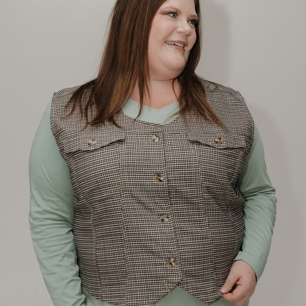 Woman wearing a checkered vest over a light green shirt against a plain background