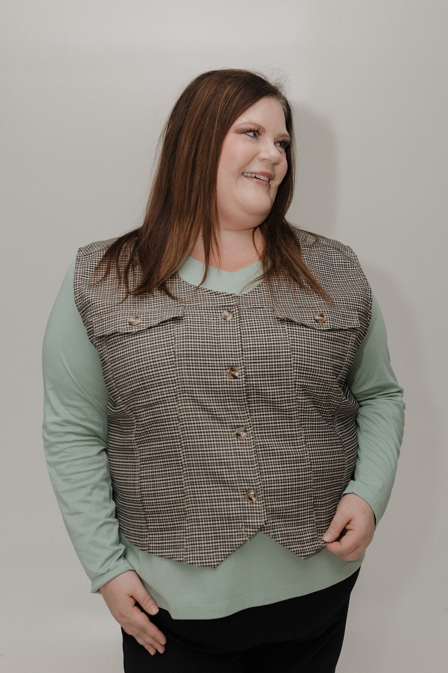Woman wearing a checkered vest over a light green shirt against a plain background