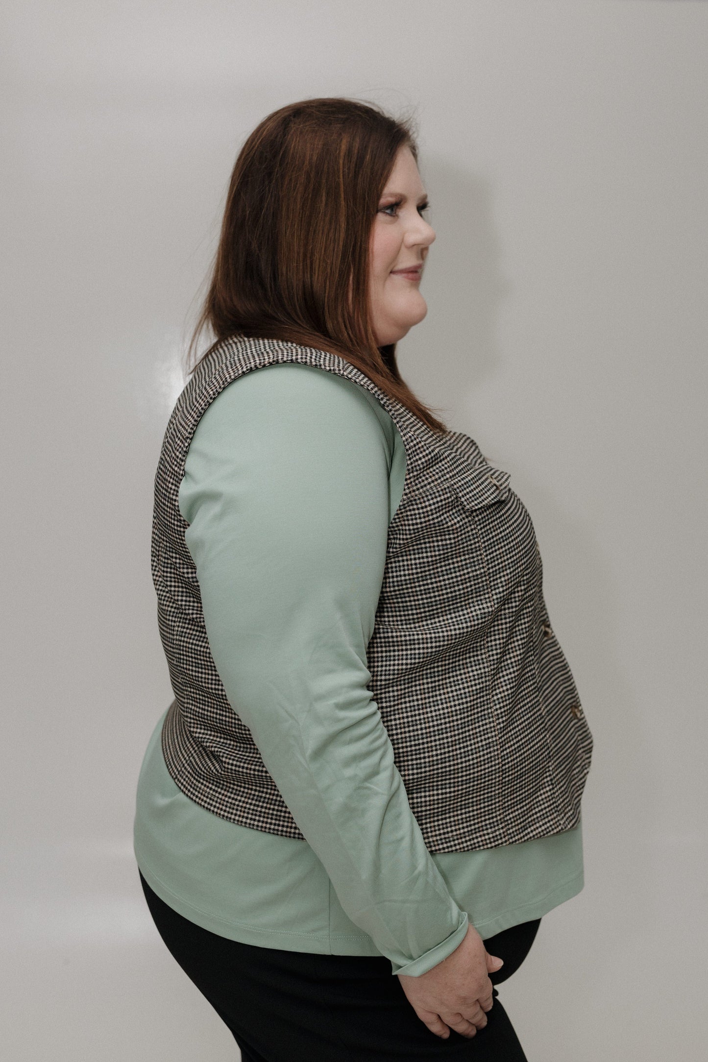 Woman wearing a patterned vest over a light green shirt against a plain background